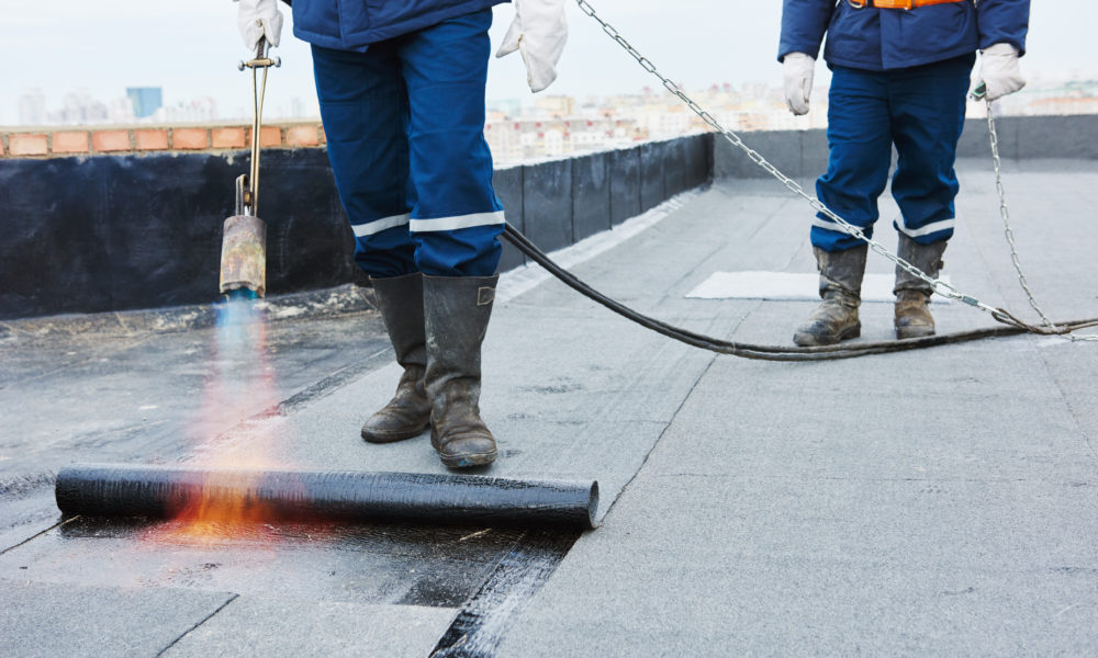 Flat roof installation. Heating and melting bitumen roofing felt by flame torch at construction site